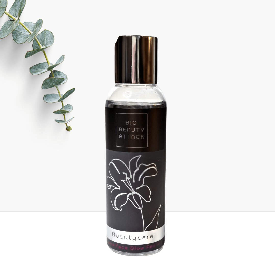 Flasche Bio Beauty Attack Face Glow Peeling mit schwarzem Etikett, silber-schwarzem Deckel und Blütenmotiv, dekoriert mit Eukalyptuszweig auf weißem Hintergrund.