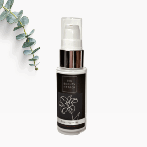 Flasche Bio Beauty Attack Gesichtscreme mit schwarzem Etikett, silbernem Pumpverschluss und Blütenmotiv, dekoriert mit Eukalyptuszweig auf weißem Hintergrund.