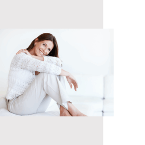 Frau mit langen braunen Haaren sitzt entspannt auf einem Sofa, lächelt und blickt freundlich in die Kamera