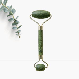 Grüner Jade-Roller aus Naturstein für Gesichtsmassage, daneben ein Eukalyptuszweig, auf weißem Hintergrund.