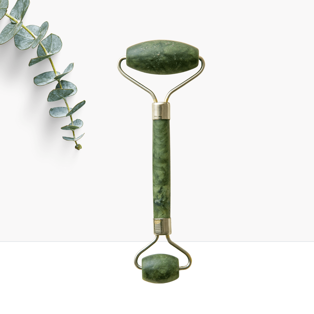 Grüner Jade-Roller aus Naturstein für Gesichtsmassage, daneben ein Eukalyptuszweig, auf weißem Hintergrund.