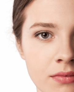 Eine junge Frau mit glatter, gepflegter Haut schaut ruhig in die Kamera. Nur eine Gesichtshälfte ist sichtbar. Das Bild vermittelt Ruhe