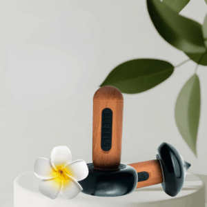 Zwei ELEEELS Wärme-Stäbe liegen auf weißen Steinen mit Blüten. Moderne Hot-Stone-Technologie für Massage, Wellness und Tiefenentspannung in Gütersloh.