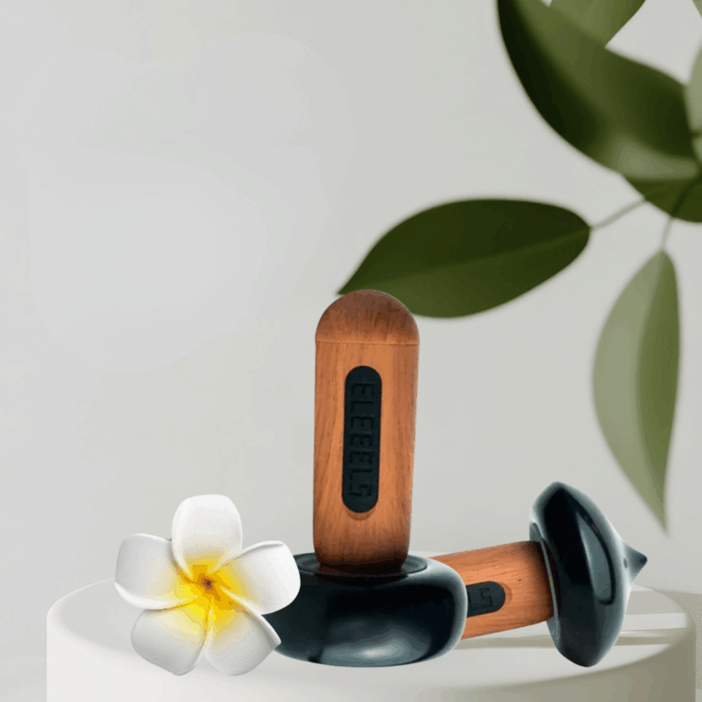 Zwei ELEEELS Wärme-Stäbe liegen auf weißen Steinen mit Blüten. Moderne Hot-Stone-Technologie für Massage, Wellness und Tiefenentspannung in Gütersloh.