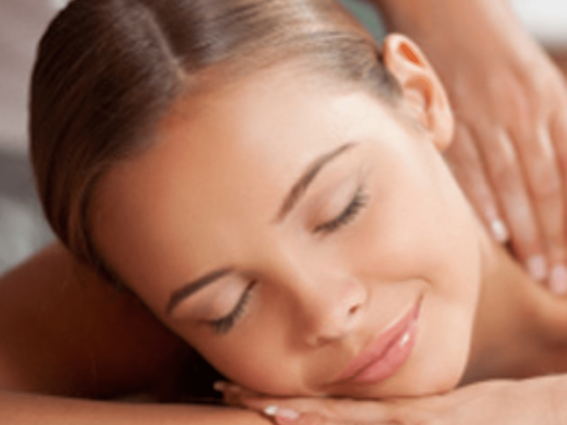 Eine Frau liegt entspannt mit geschlossenen Augen auf der Massagebank, während ihre Schultern sanft massiert werden. Das Bild vermittelt Ruhe, Wärme und Entspannung während einer professionellen Rückenmassage in Gütersloh.